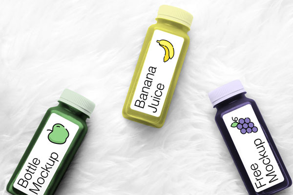 Mockup Featuring Three Bottles of Juice Laying on a Fluffy Background FREE PSD